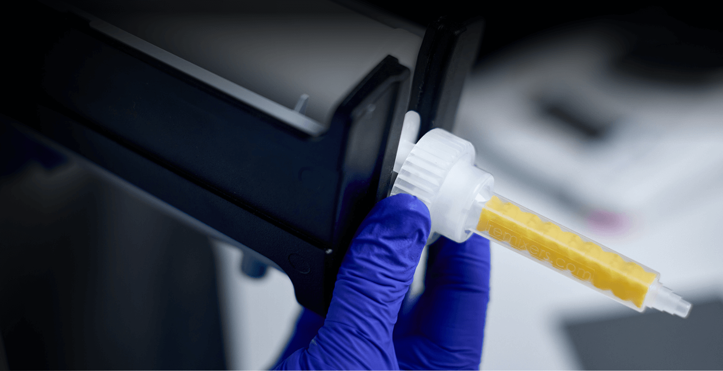 Gloved hand inserting yellow Re Mixers static mixer nozzle into 2K adhesive dispenser